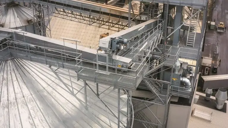Sicht von Oben auf ein Silo, überdachte Förderbänder, Treppen und Inustriehallen-Decken.