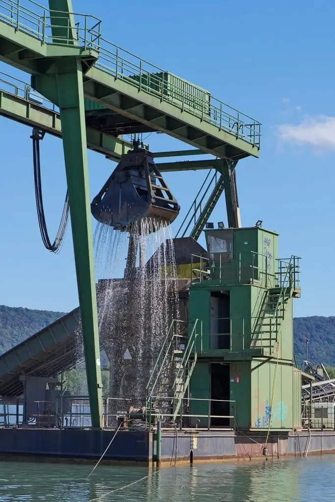 Auf einem See ist eine Kranplattform, Es wurde gerade etwas aus dem See gehoben. Aus der Baggerkralle läuft Wasser.