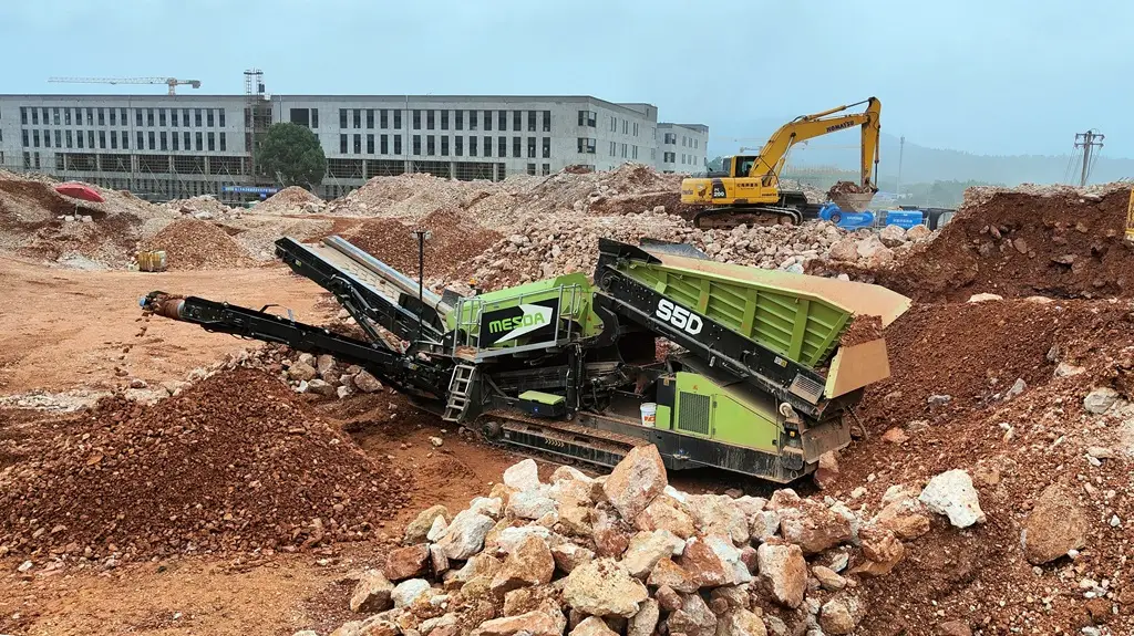 Grobstücksiebmaschine an Baustelle im Hintergund ein Bagger und ein Bürogebäude