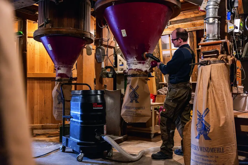 Absacken unter einem Silo in einer Mühle mit Mitarbeiter der über der Absackanlage absaugt.