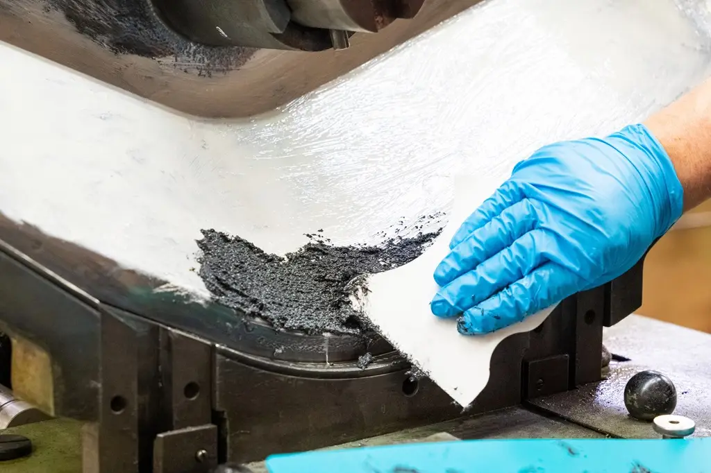 Hand in blauem Gummihandschuh trägt auf eine metallene, nach oben gebogene Fläche Plastik-Stahl WP auf.