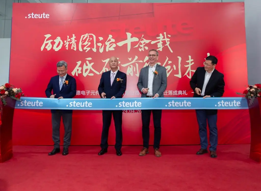 4 Herren stehen vor einer roten Wand auf der in Chinesisch und deutsch steute steht. Sie scheiden vor sich ein blaues Band mit steute Schriftzug durch.
