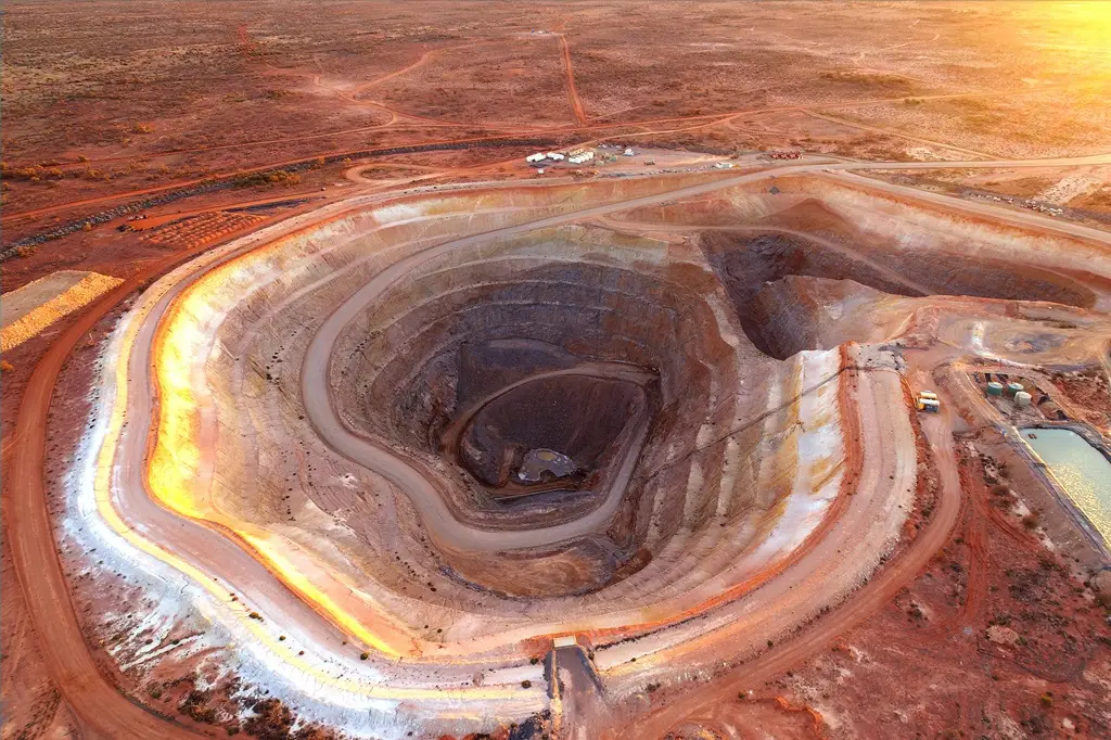 Tiefe Tagebau-Goldmine mit Erde, die rötlich ist und durch den rechts vermuteten Sonnenuntergang zum Teil golden glänzt.