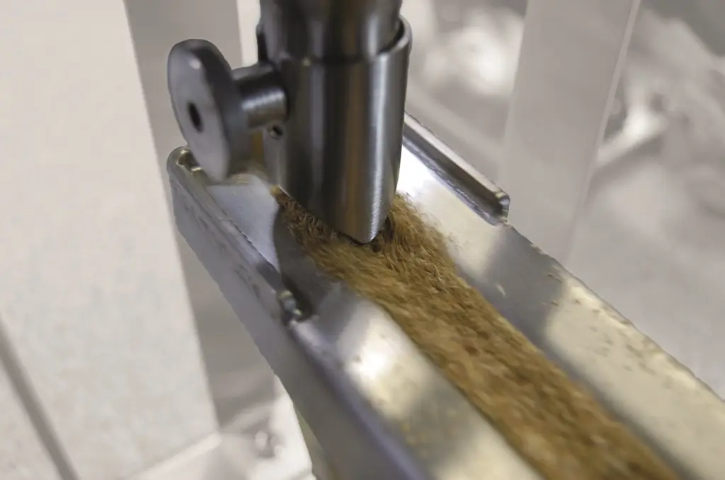 Holzartiges Schüttgut wird durch Vibrationstechnik im Handling optimiert über eine Tülle auf eine Laufrinne gegeben.
