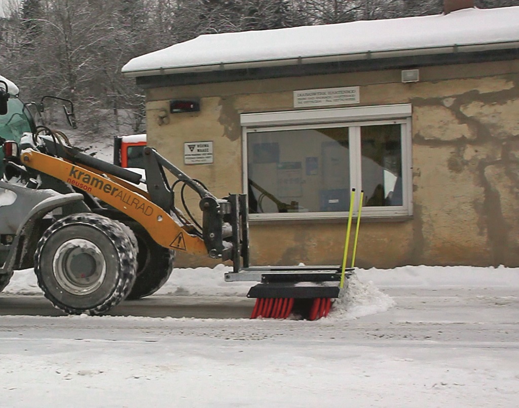 Radlader hat einen Schneebesen vor den Reifen und schiebt Schnee vom Hof