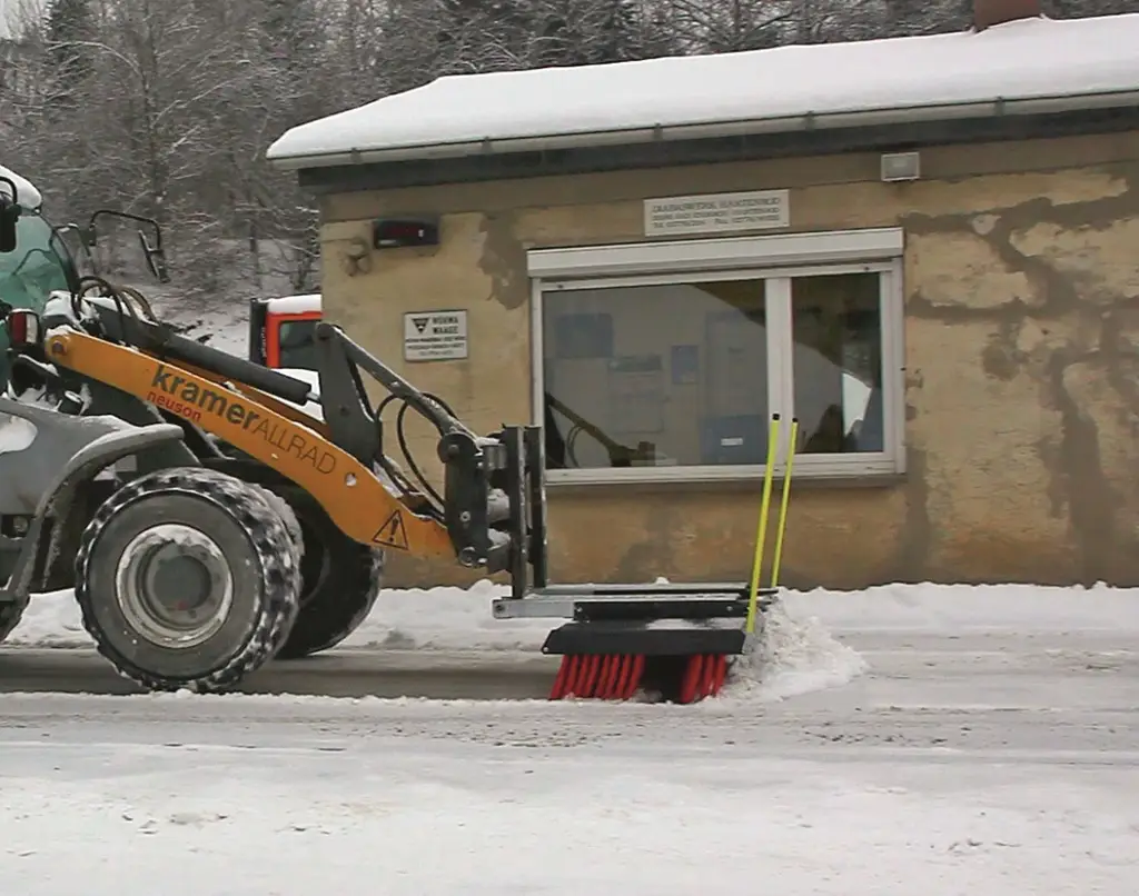 Radlader hat einen Schneebesen vor den Reifen und schiebt Schnee vom Hof