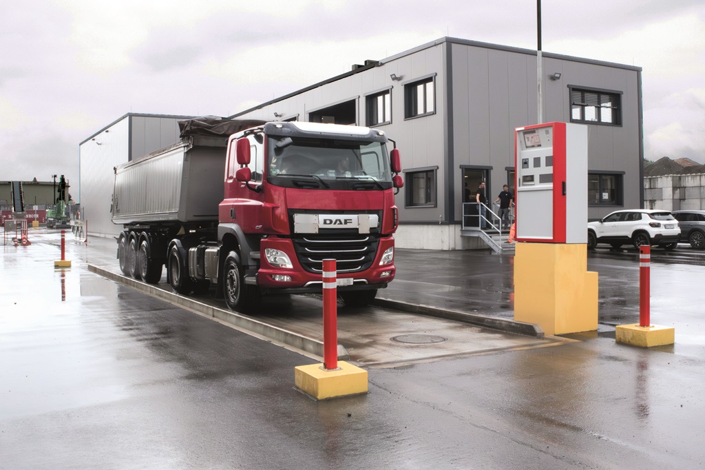 Lastwagen fährt auf eine Waage. Das Wägeterminal ist in Höhe des Fahrers.