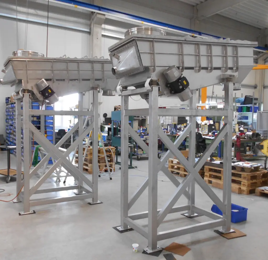 Zwei Vibrationsrinnen der NetterVibration auf hohem Gestellen in der Produktionshalle des Herstellers