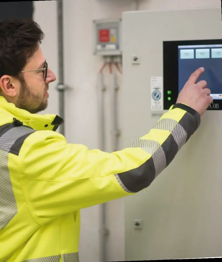 Arbeiterin einer gelben Schutzjacke bedient ein digitales Panel.