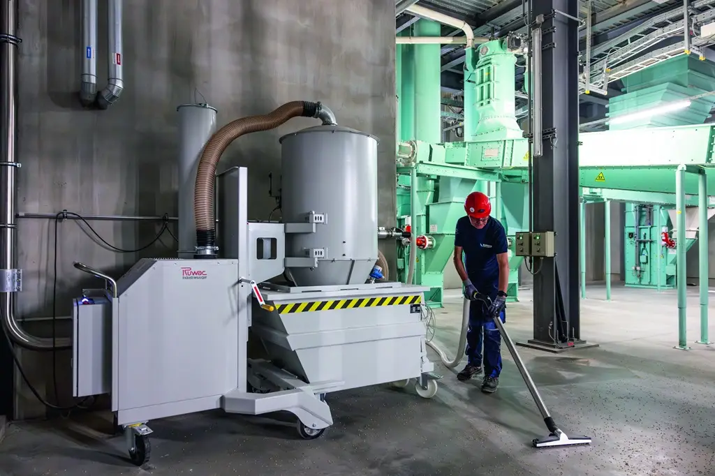Mitarbeiter saugt in einer Industriehalle Partikel vom Boden