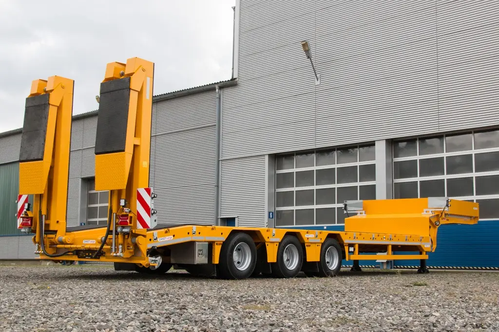 Sattel-Tieflader vor Industrierolltor. Die Auffahrtrampe ist hochgeklappt und besteht aus 2 Schienen.