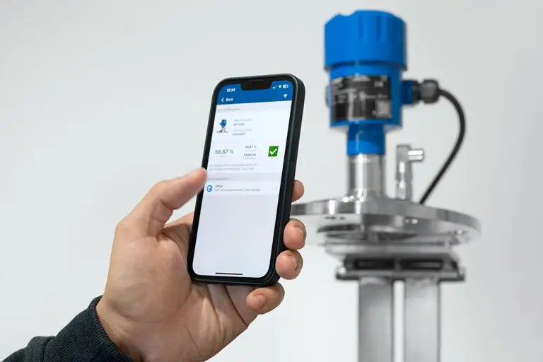 Hand mit Mobiltelefon im Vordergrund und im Hintergrund ein Sensor.