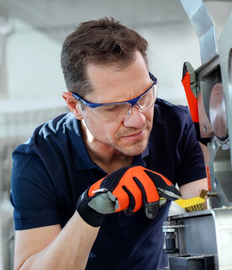 Mitarbeiter reinigt Industriearbeitsplatz mit einer kleine Metallbürste
