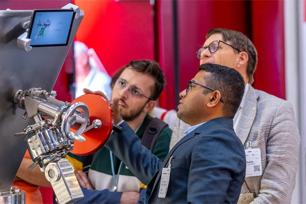 Drei Personen schauen sich auf einem Messestand eine Innovation aus dem Verfahrenstechnischen Bereich an.