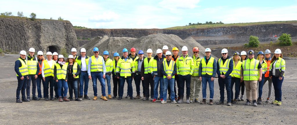 Gruppenfoto eines Vor-Ort-Treffen mit gelben und orangen Warnwesten in einem Tagbauwerk