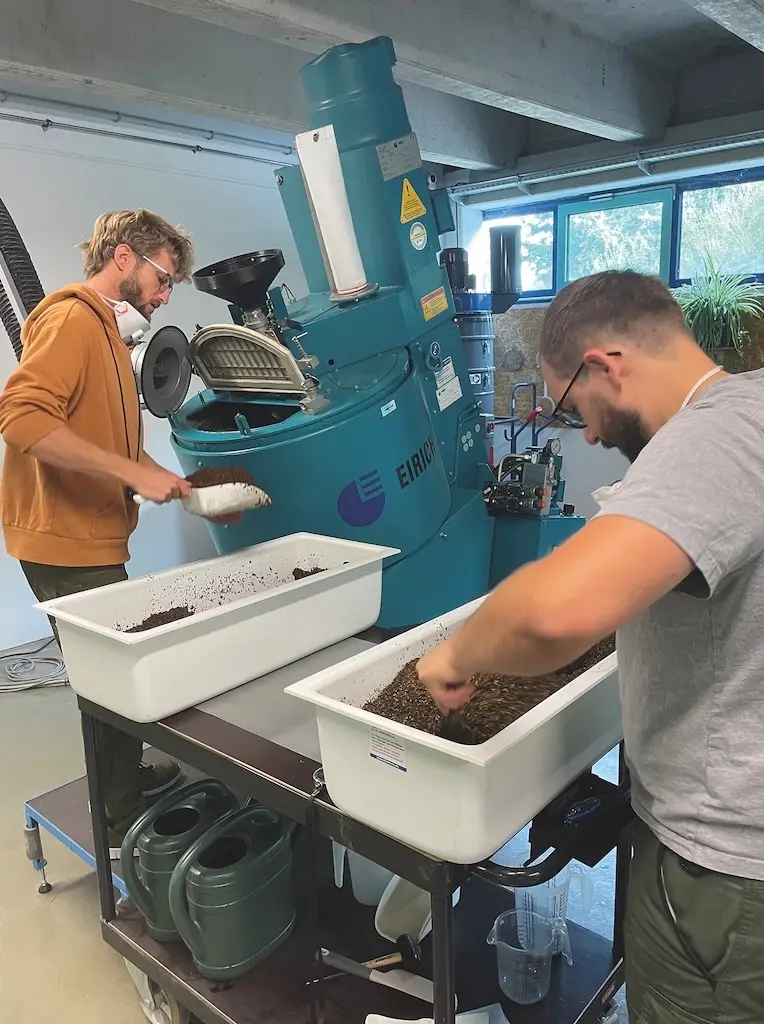 Zwei Männer arbeiten mit einem Samengemisch an einer großen Maschiene um Samenpellets herzustellen.