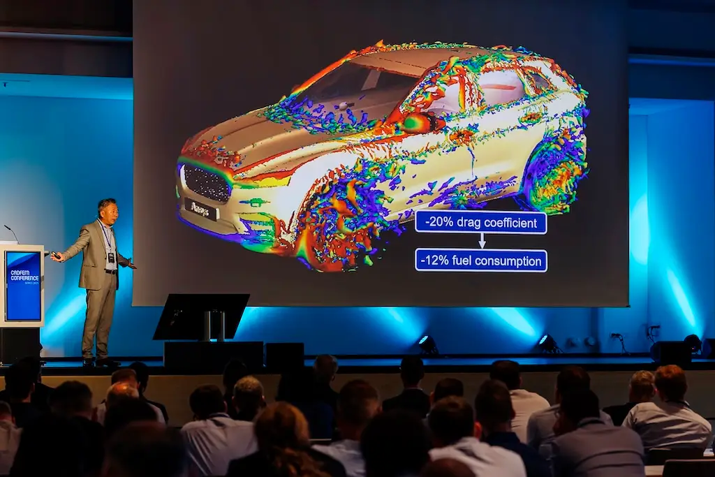 Konferenz bei der ein Mann auf der Bühne steht und ein Slide von einem Auto zeigt