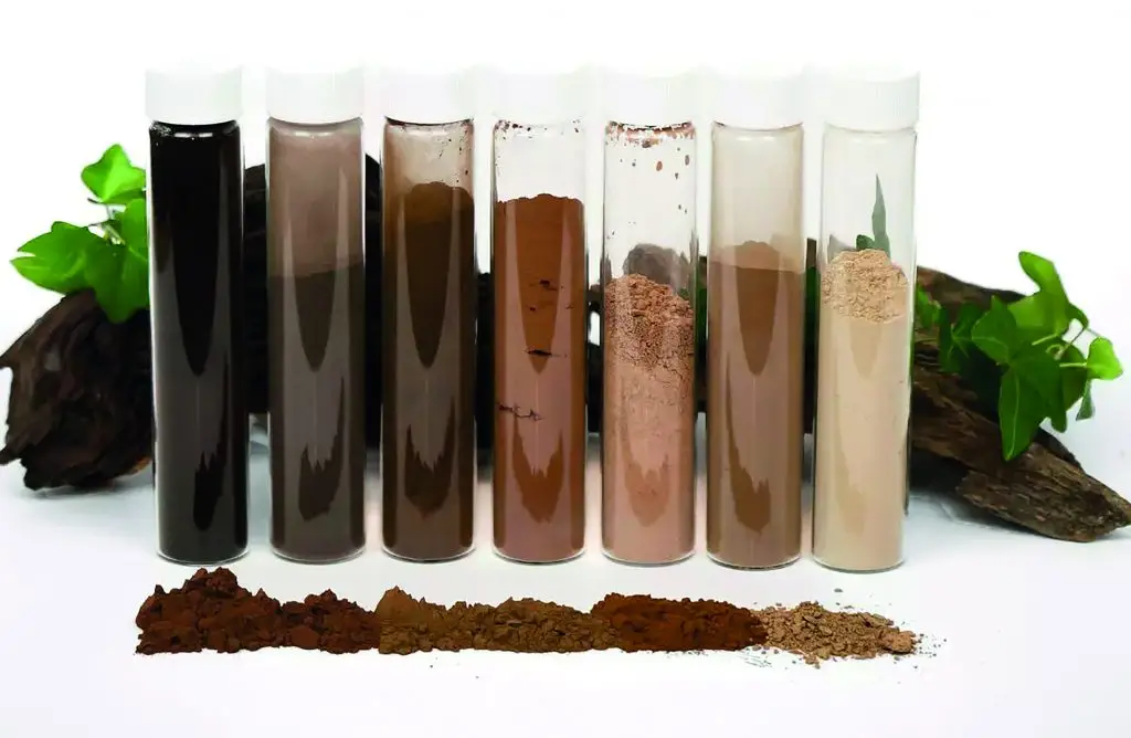 Sieben Gläser mit Deckel mit Pulverfüllung in unterschiedlichen Brauntönen. Davor ein streifen der Pulver und im Hintergrund ein stück Holz