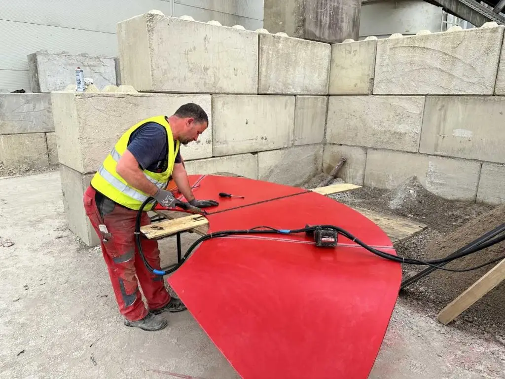 Mann arbeitet an rotem Metallbauteil in einer Industriehalle