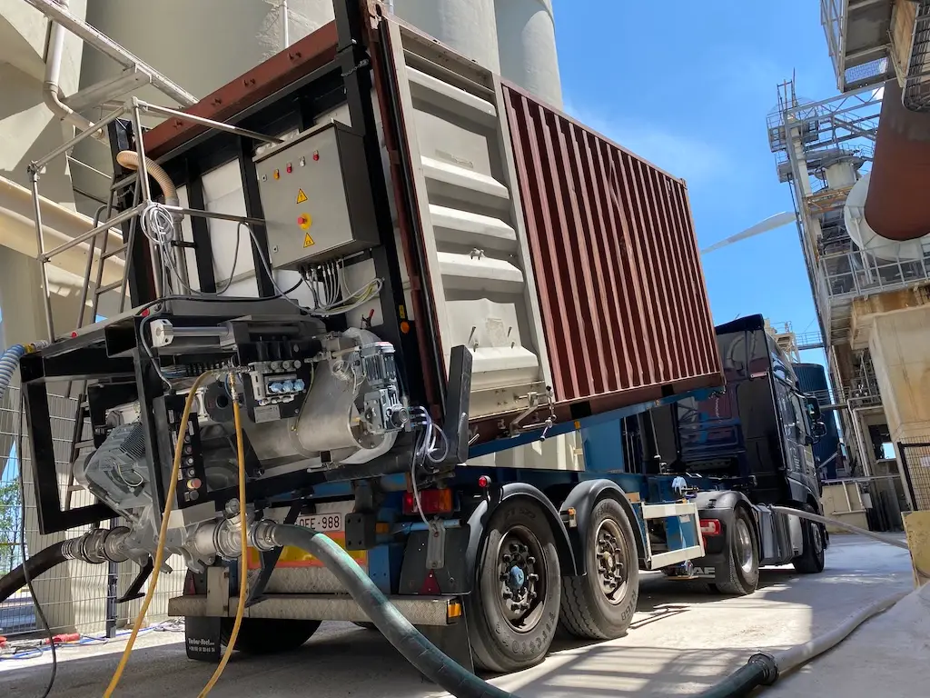 LKW der mit Container beladen ist neben Silos.