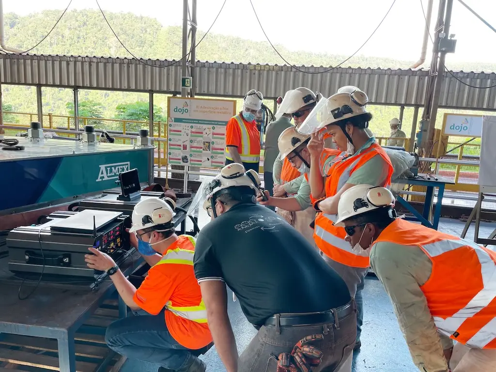 Einige Personen in Arbeitskleidung gucken auf einen kleinen Bildschirm