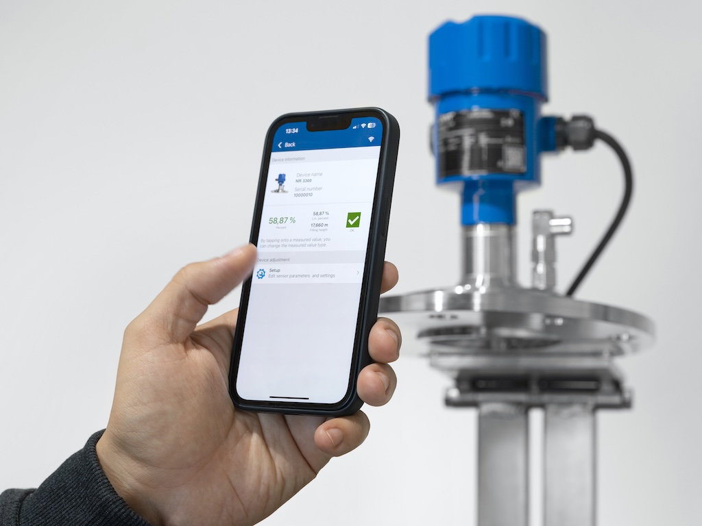 Hand mit Handy. Im Hintergrund ein Blauer Sensor