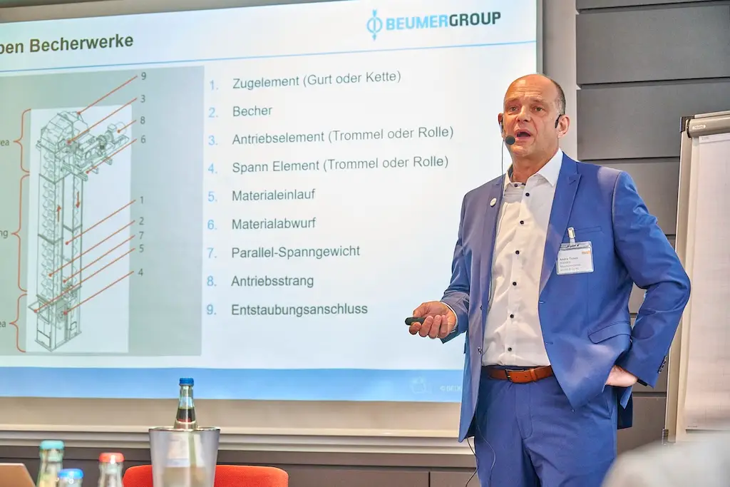 Mann in blauem Anzug, der vor einer Leinwand steht und einen Vortrag hält.