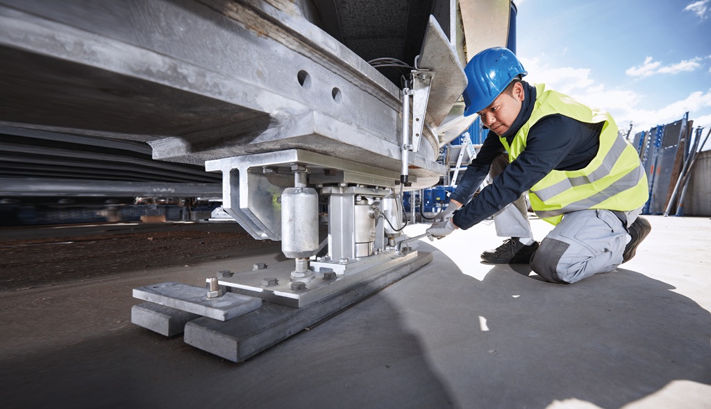 Ein Techniker arbeitet an einer Wägezelle, die in einem Außengelände steht.