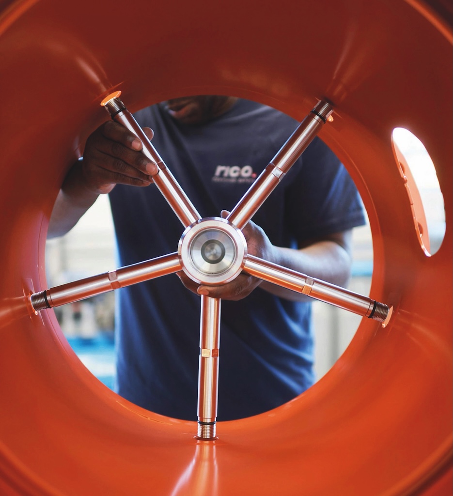 Foto innerhalb eines roten Rohres mit einem Metallventil, welches von einem Mann in das Rohr eingesetzt wird.