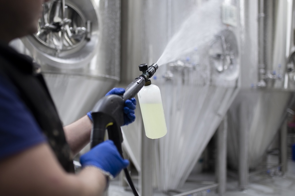 Arbeiter halten eine Hochdruckreinigungspistole in der Hand und sprühen Schaum auf die Geräte in der Fabrik.