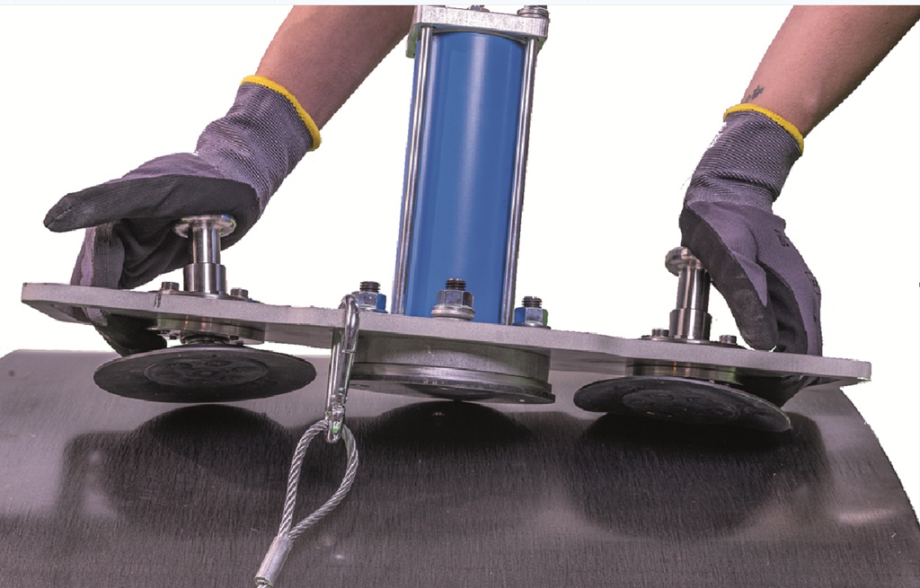 Ein industrieller mobiler Kloppfer wird an einer metallenen Fläche angebracht. Man sieht den Klopfer und zwei behandschuhte Hände.