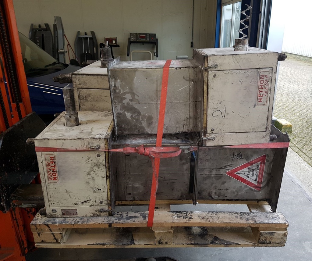 Auf einer Holzpalette stehen mehrere stark verschmutzte industrielle Hethon‑Förderbehälter und Schüttgutmodule, die mit roten Spanngurten gesichert sind. Die gebrauchten Metallkomponenten befinden sich in einer Werkstatt- oder Lagerumgebung, bereit für Transport, Reinigung oder Refurbishmen