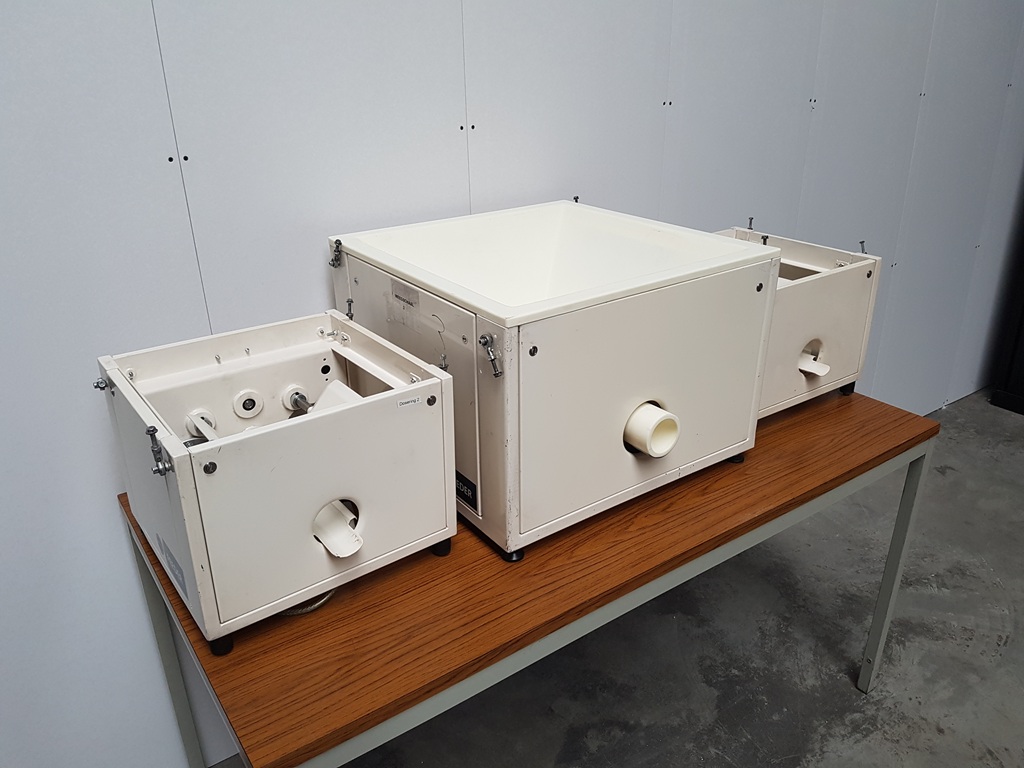 Drei weiße Hethon‑Schüttgutdosierer in unterschiedlichen Baugrößen stehen gereinigt und montiert auf einem Holztisch in einer Werkstatt. Die rechteckigen Kunststoffgehäuse besitzen jeweils einen frontseitigen Auslass und sind für präzise Pulver‑ und Granulatdosierung ausgelegt