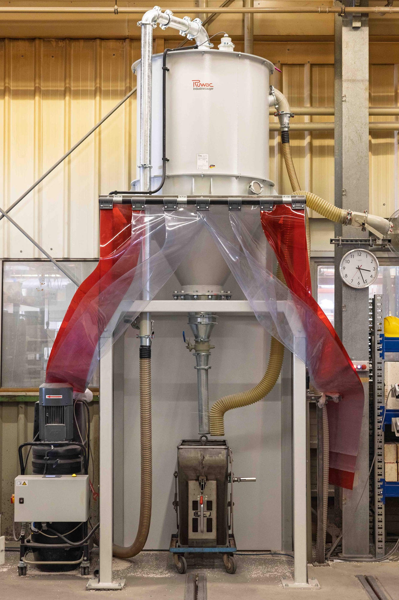 Industrieanwendung beim Abfüllvorgang. Ein Silo fördert pneumatisch in ein anderes Gefäß. die Abfüllstation ist zum Staubschutz eingehaust, aber der Vorhang weggeschoben.