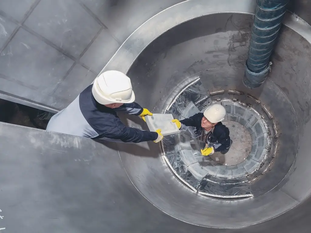 Vogelperspektive auf zwei Techniker in Helmen und gelben Handschuhen beim Einbau von Verschleißschutzplatten in den Einlaufbereich eines großen Industriezyklons
