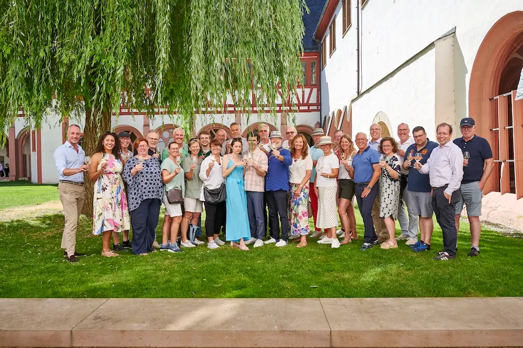 Gruppenfoto der Teilnehmenden des DSIV-Sommerfests mit Weingläsern auf einer Rasenfläche vor einem historischen Gebäude