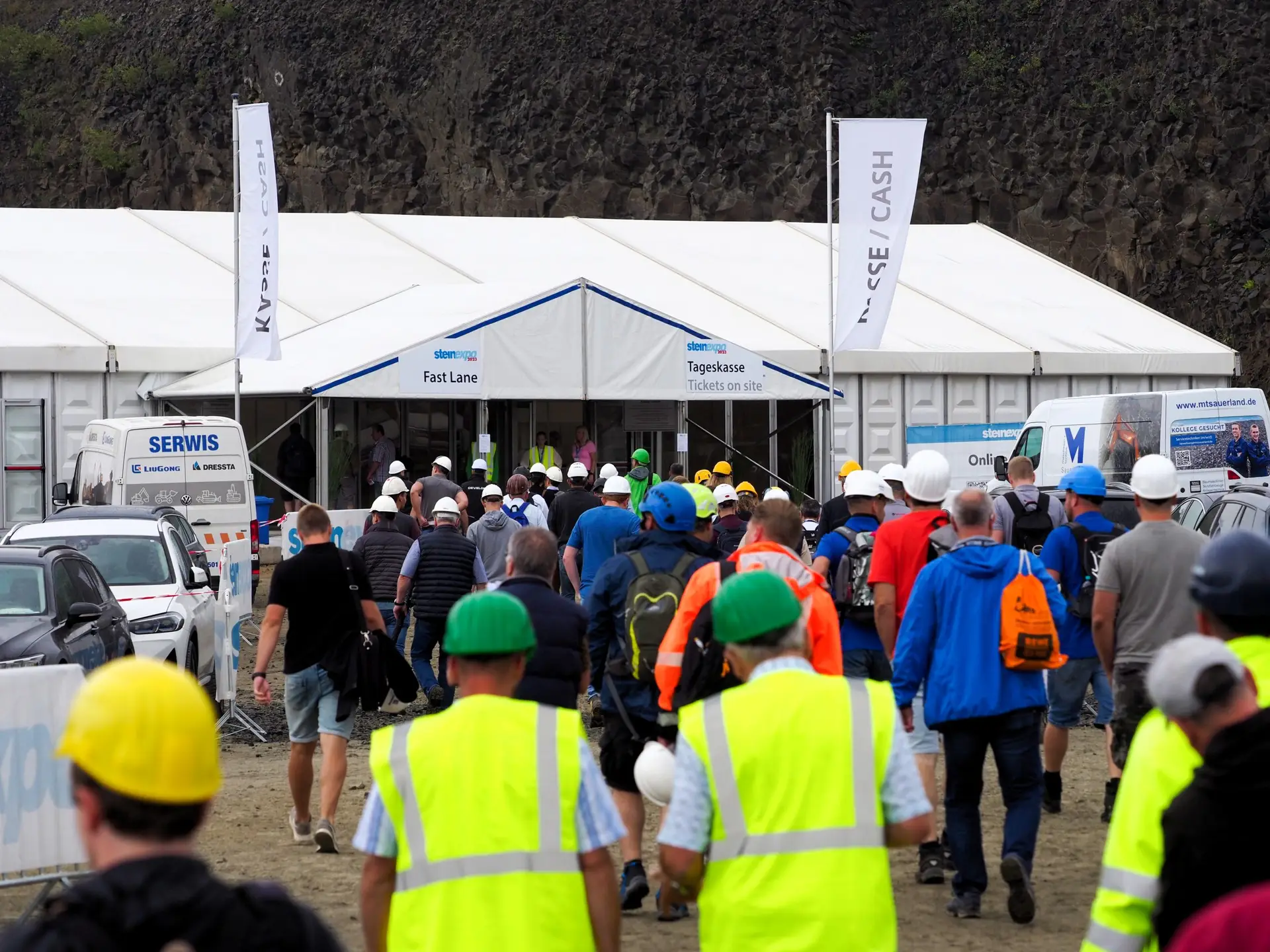 Besucher der steinexpo betreten den Eingangsbereich der Messe im Basaltsteinbruch und tragen die vorgeschriebenen Schutzhelme.