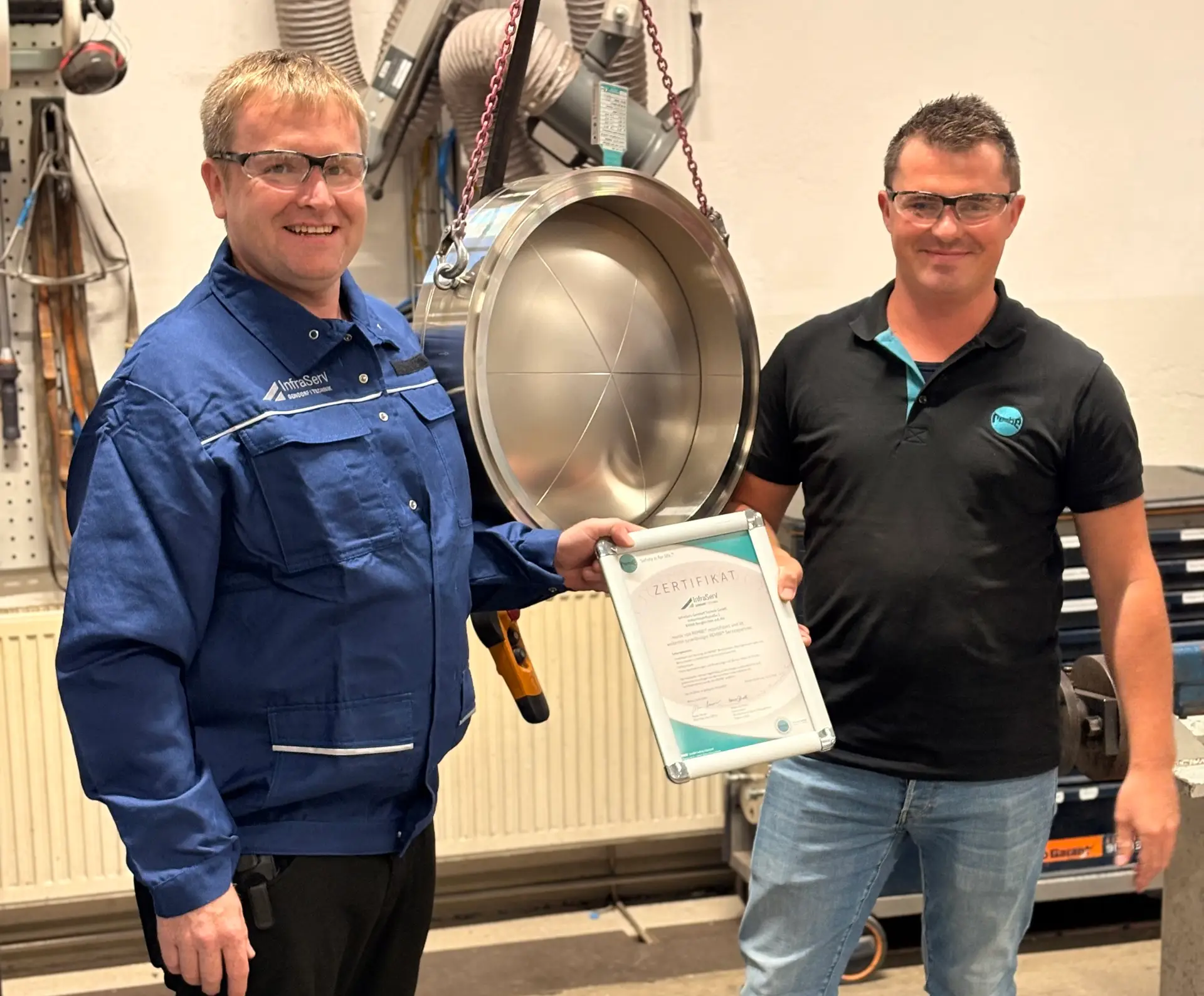 Übergabe der REMBE-Zertifizierungsurkunde an InfraServ Gendorf Technik vor einer REMBE-Berstscheibe in einer Werkstattumgebung.