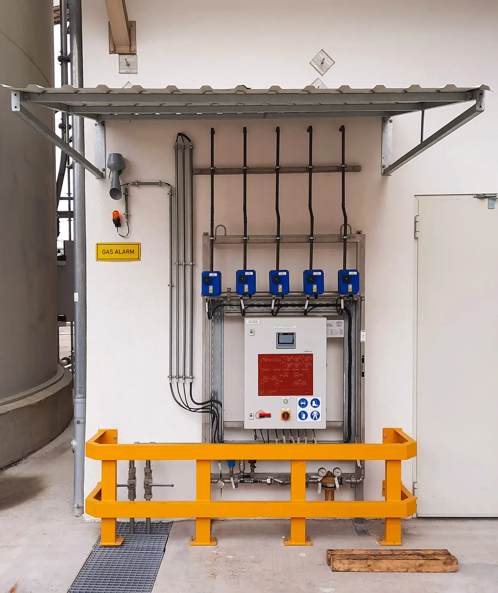 Wandmontierte Ventilstation mit fünf blauen Gassensoren, Schaltschrank, Warnleuchte und Schild „Gas Alarm" hinter einem gelben Schutzbügel