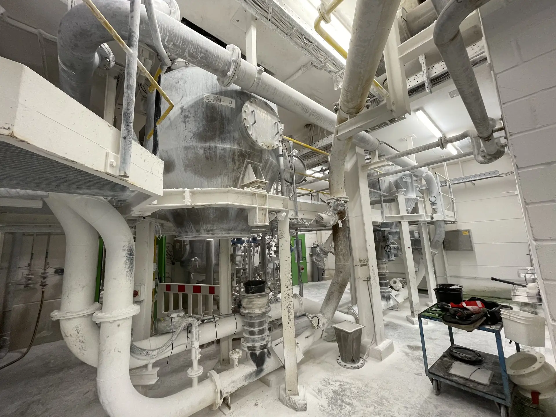 Von Pulverstaub bedeckter Prozessbereich mit Behälter, Rohrleitungen und Fördersystemen in einer Anlage der Spezialchemie
