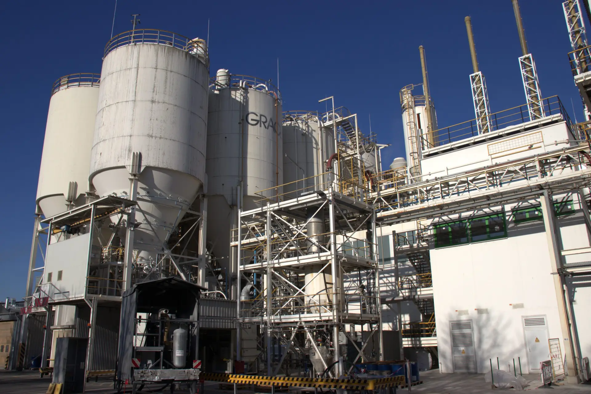 Silogruppe mit Stahlkonstruktion, Rohrleitungen und Bühnen auf dem Gelände eines Chemiewerks vor blauem Himmel
