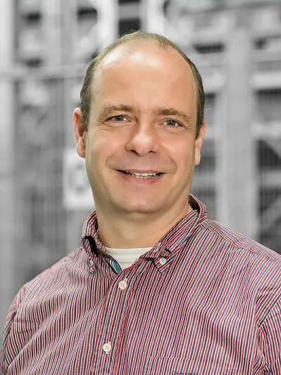 Rainer Schulz, Geschäftsführer der sysmat GmbH, vor einem unscharfen Hintergrund mit Industrie- und Lagertechnik. (Quelle: sysmat GmbH)
