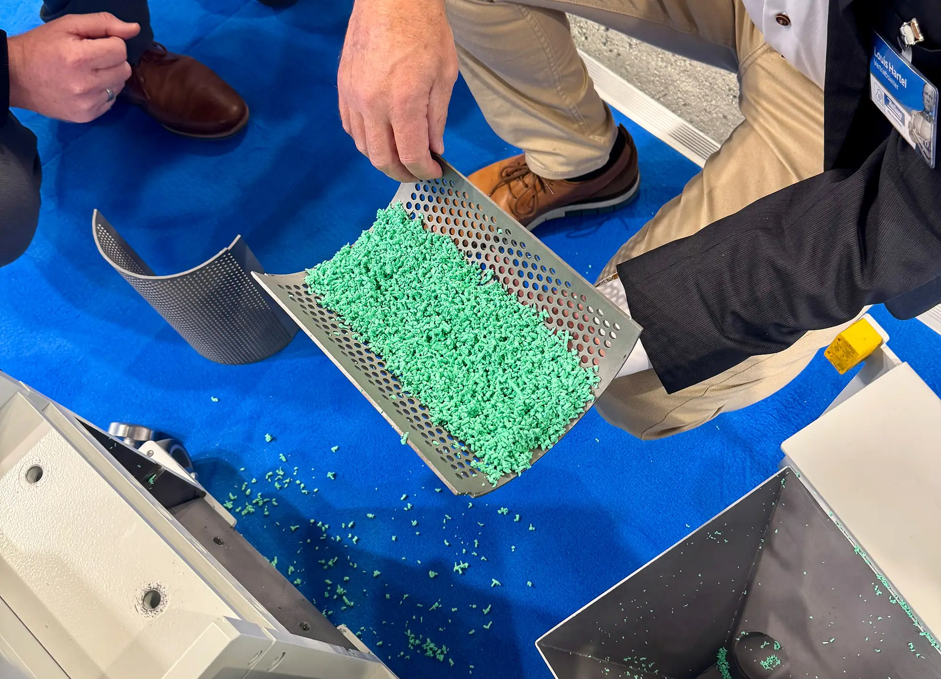 Angüsse aus grünem, ultraelastischem TPE auf einer gelochten Metallschaufel nach einem Ad-hoc-Mahlversuch auf der Fakuma 2026.